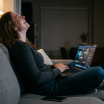 Woman laughing while watching a Hulu Watch Party on her laptop from her couch at night